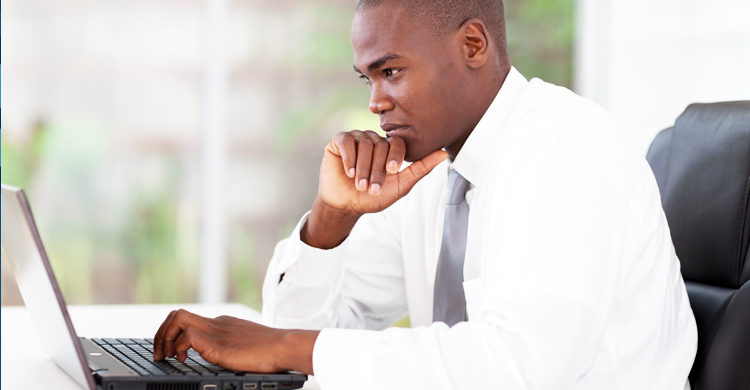 Man in white shirt and gray tie looking thoughtfully at his laptop