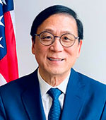 Portrait of a smiling Asian man with short black hair, round glasses, blue coat and tie and white shirt