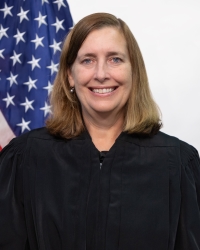 Judge Erica S. Beardsley, a smiling white woman with blonde hair wearing a judge&#039;s black robe