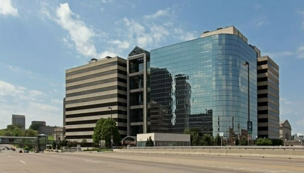 A large office building next to a highway and a pedestrian bridge with Union Station train station in background.