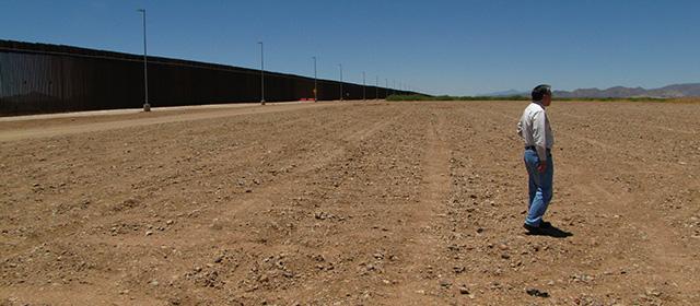 Image of a a GSA employee in front of a border wall and in the sand.