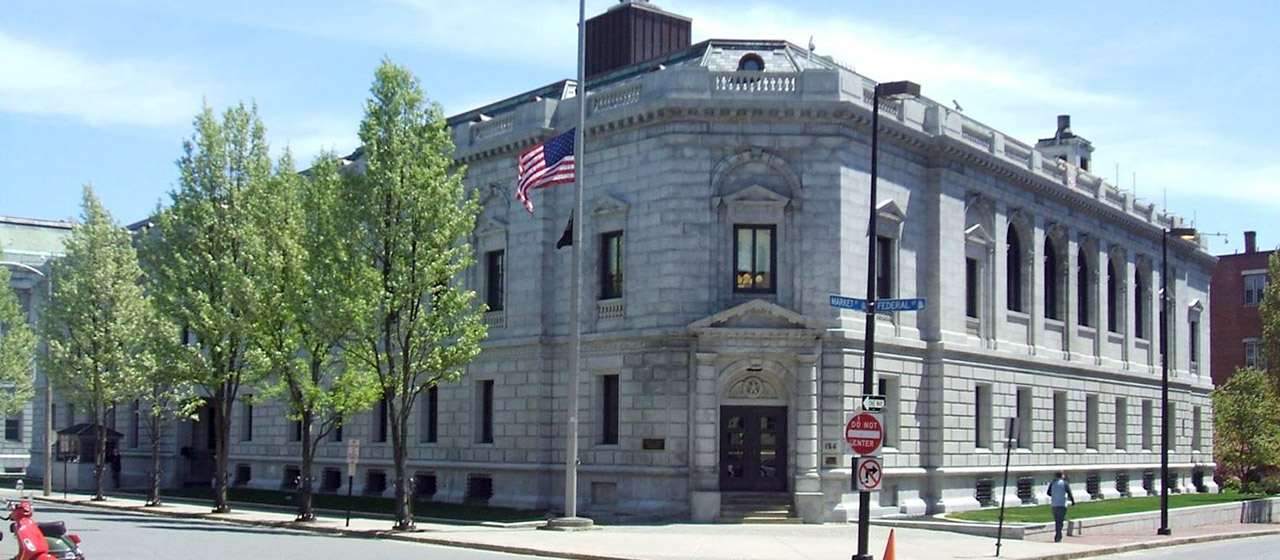 Corner view of gray stone two-level building in governmental style with U.S. flag flying at the corner entrance