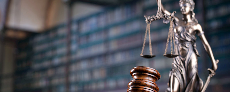 A metallic statue of blind justice holding a scale, with shelves of books behind her.