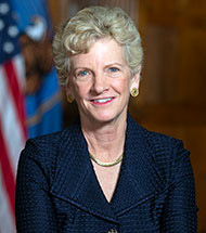 Portrait of Administrator Robin Carnahan. Robin has light hair and is wearing a blue suit standing next to the American flag.