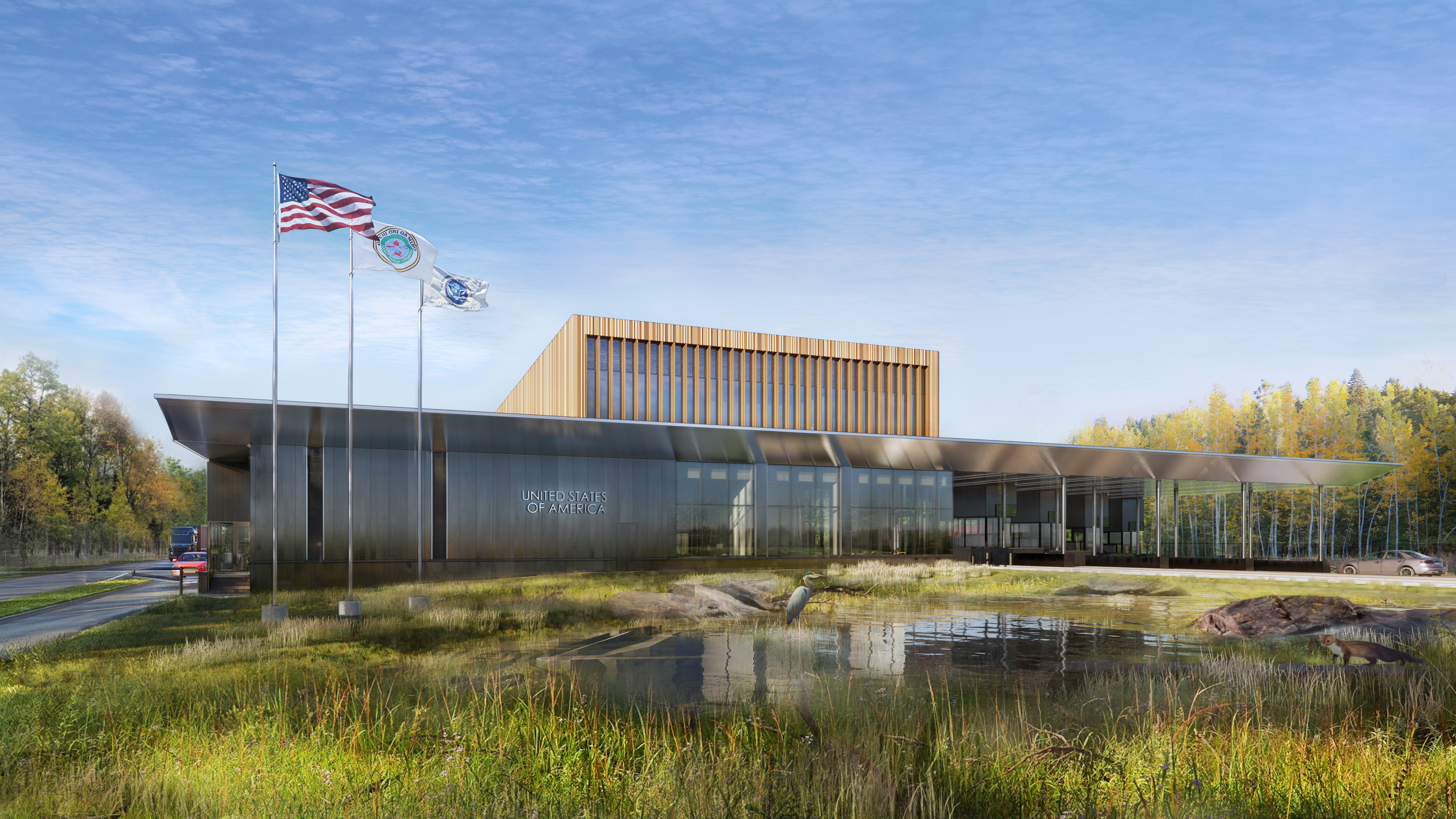 Image of 1-story grey building, with awning to the left. 3 flags fly to the right of the image. A small pond with rocks is to the front side