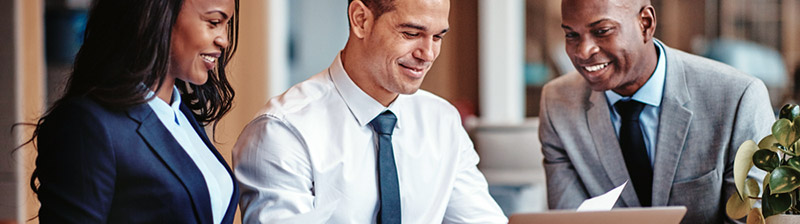 Cropped view of three smiling business people looking at a piece of paper and laptop
