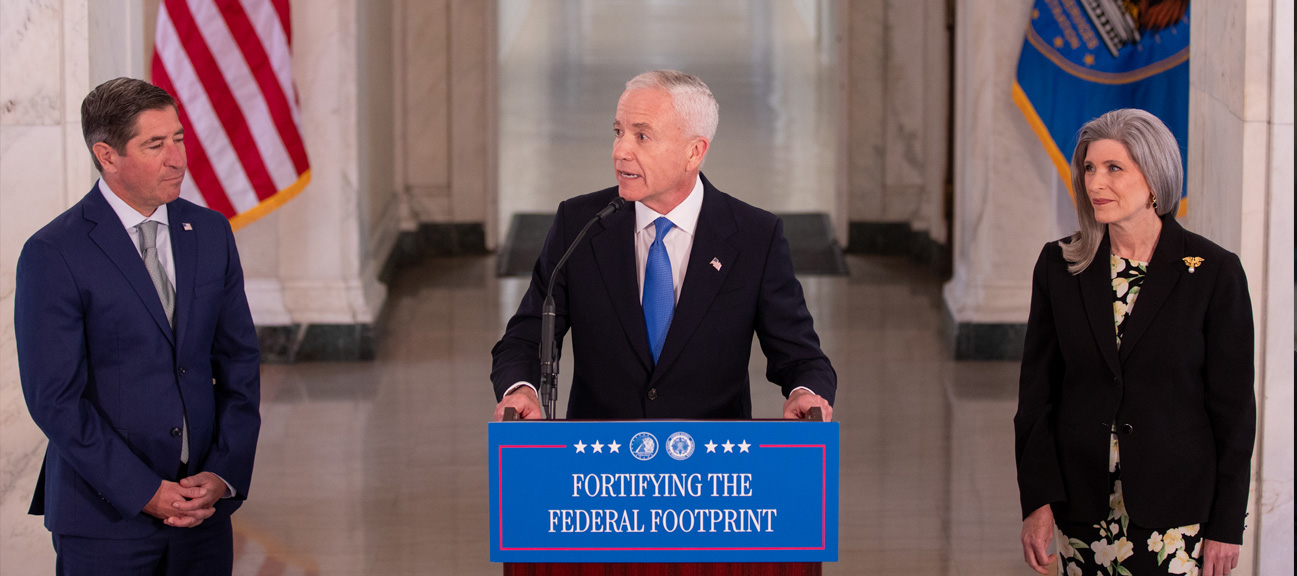 Edward C. Forst speaks at a podium displaying 'Fortifying the Federal Footprint,' flanked by a man and a woman, during an announcement event