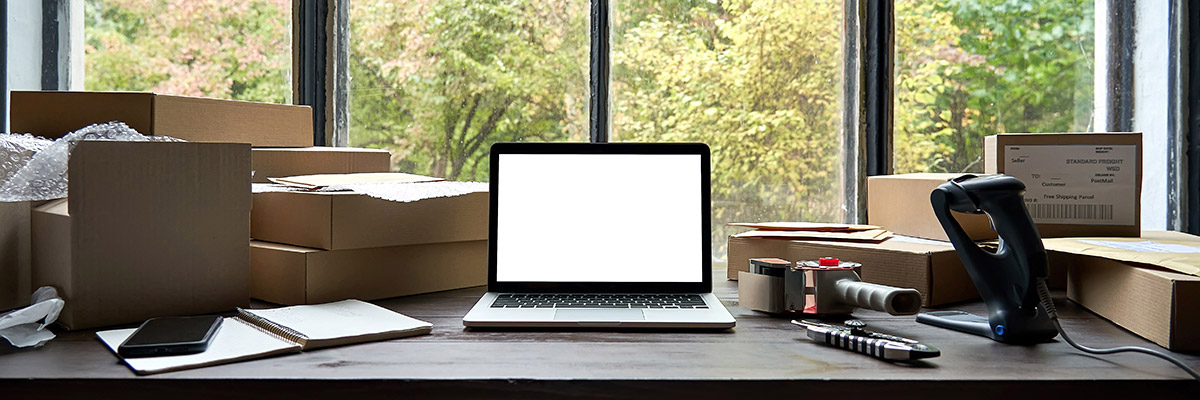 Desktop with laptop in the middle, and packing tape, papers and boxes surrounding it