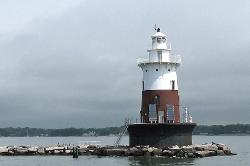 Greens Ledge Lighthouse in the middle of the ocean with rocks surrounding it