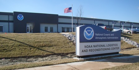 Front of new NOAA location with NOAA Seal on the building behind a sign saying National Oceanic and Atmospheric Administration NOAA National Logistics and Reconditioning Center