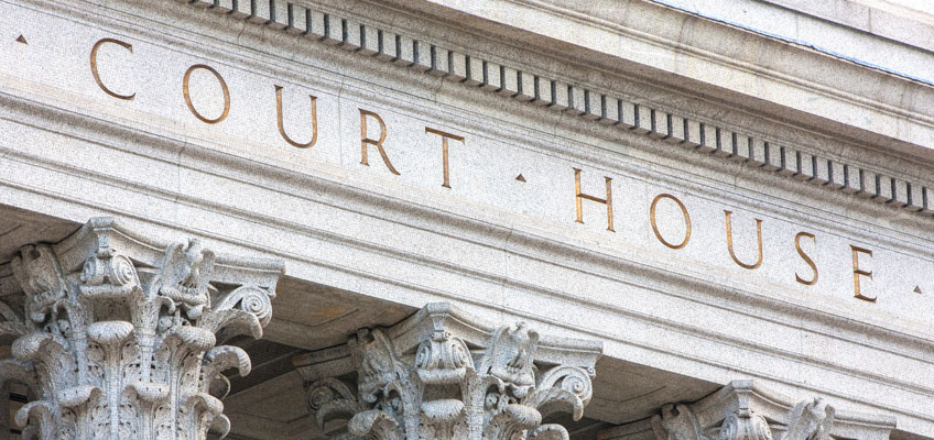 The word Courthouse embossed in gold on the off-white granite facade of a courthouse.
