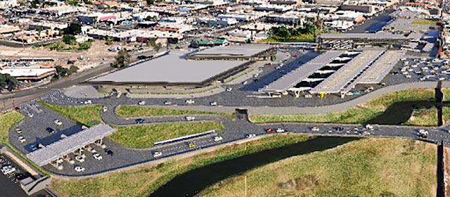 Aerial view of a group of low buildings, with roads and traffic lanes and covered booth area, a parking lot, and areas of green grass and a river in the foreview