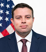 Portrait of Andrew Tulli, who wears a navy jacket, white shirt and purple tie