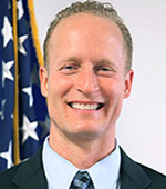 Headshot of David Shiveshort. David has short light hair and is wearing a blue tie and dark jacket.