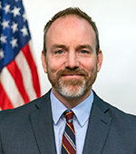 Smiling bearded person in dark blue jacket and maroon tie