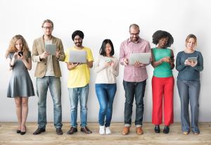 A diverse group of people standing in a line using different technologies