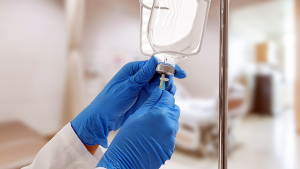 A close-up image of a healthcare professional in blue gloves adjusting an IV drip in a hospital setting