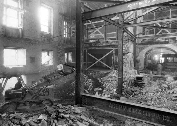 Black and white image of a young man on a construction vehicle inside the White House with rubble and exposed beams