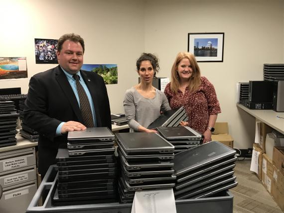 RA Averiall and school reps standing next to over 100 donated laptops on cart 