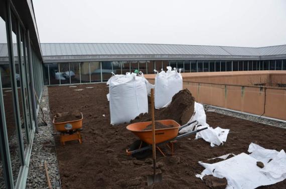 Photo a planted roof installation. The flat roof is covered in a layer of soil, with large, crane-lifted soil bags visible in the foreground
