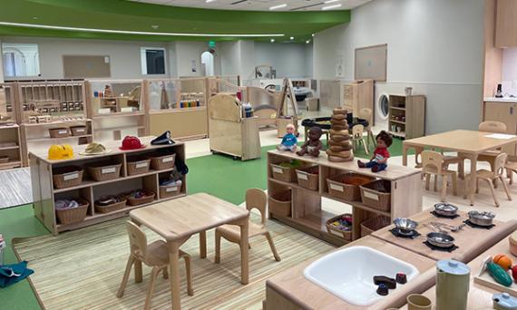 A play room in a child-care center, with blond-wood shelving and furniture, and green flooring and ceiling, with toys and learning materials
