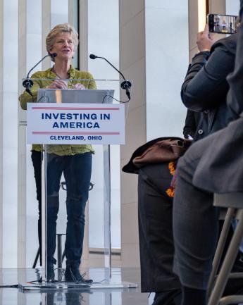 Medium shot of Administrator Carnahan at lectern with sign &quot;Investing in America&quot; talking to press at Stokes Courthouse
