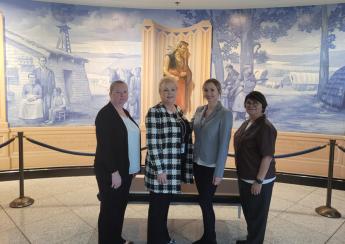 Four women in business casual attire standing in front of painted mural