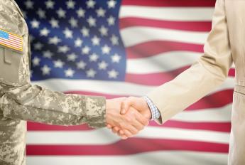 Image of a soldier and businessperson shaking hands with flag in background