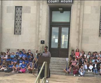 Woman at podium on Wichita Court House steps surrounded by schoolchildren