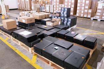 Palettes of laptops and boxes stacked in a warehouse with a cement floor