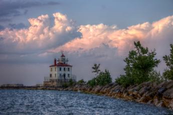 Multicolored clouds above a white lighthouse with a red roof on the bank of the water