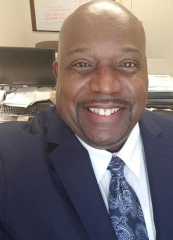 Selfie of TC Harrison at his desk. He is smiling and wearing a suit