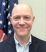 Photo of a man with the American flag seen behind his right shoulder.