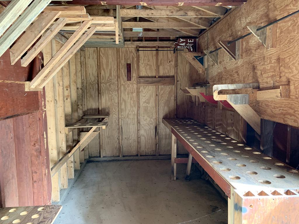 Unfinished room interior with wooden walls and ceiling, and cement floor, and a table along one side with holes in the top