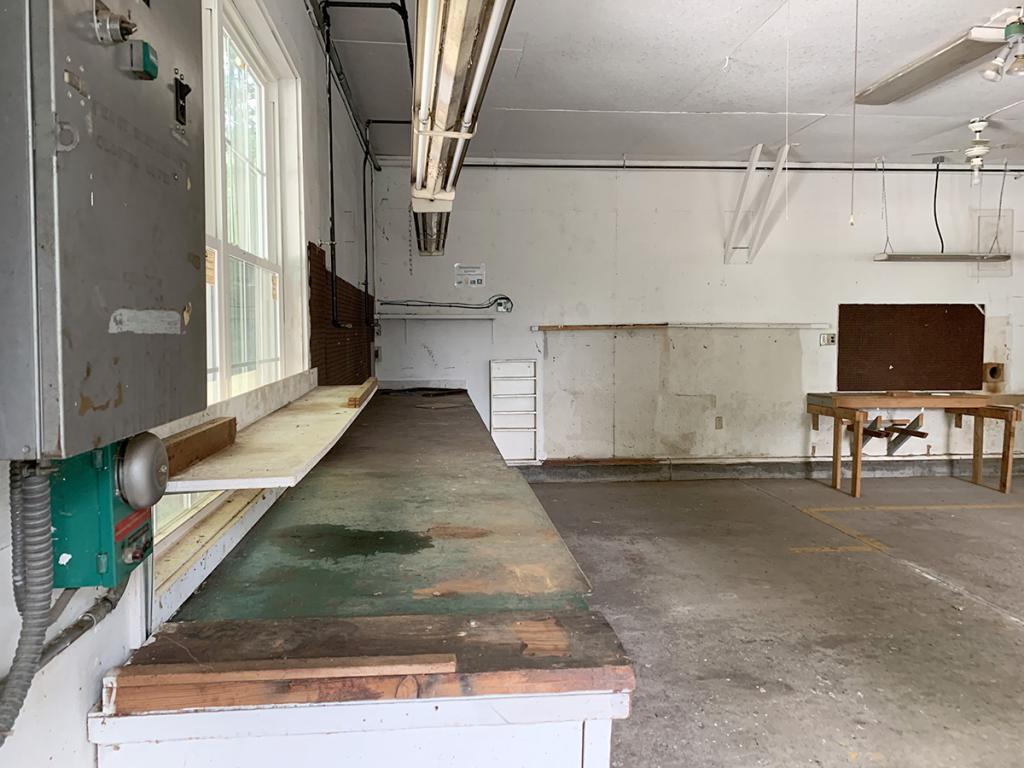 Large, garage-like room interior with white walls, built-in tables along some walls, and cement floor