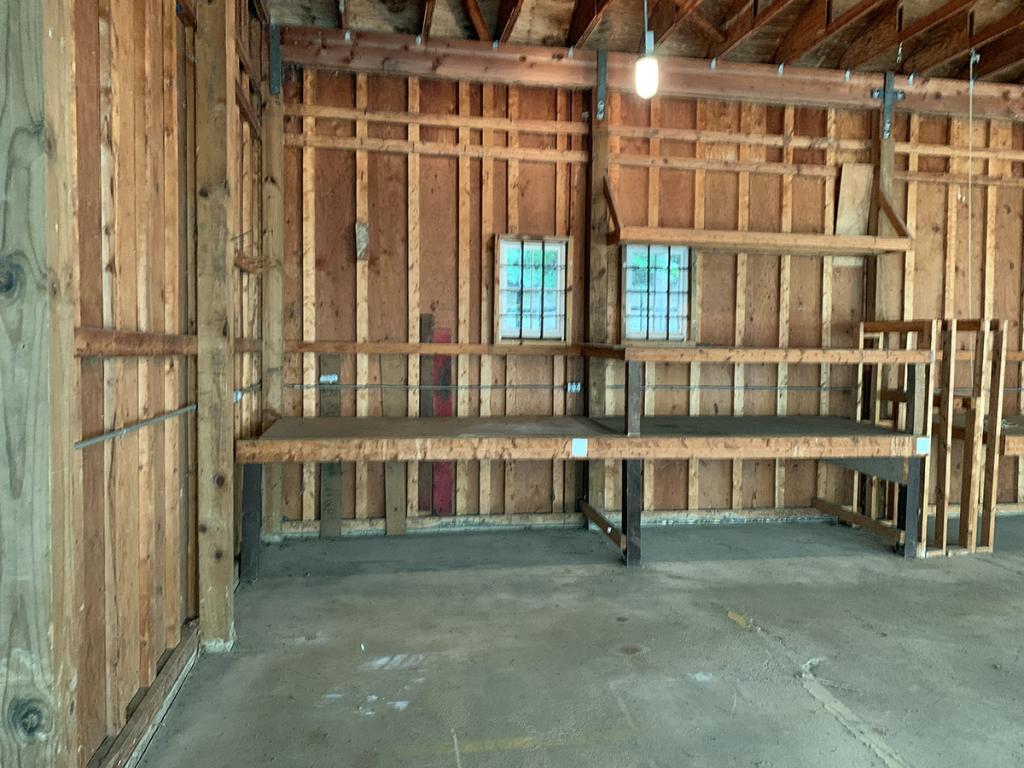 Unfinished room interior with plywood and 2-by-4 walls and ceiling, and a cement floor, with 2 small windows