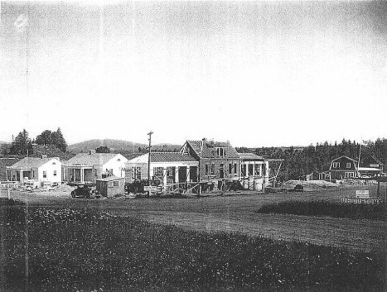 black and white photo of older houses in the background with cars parked in front of them