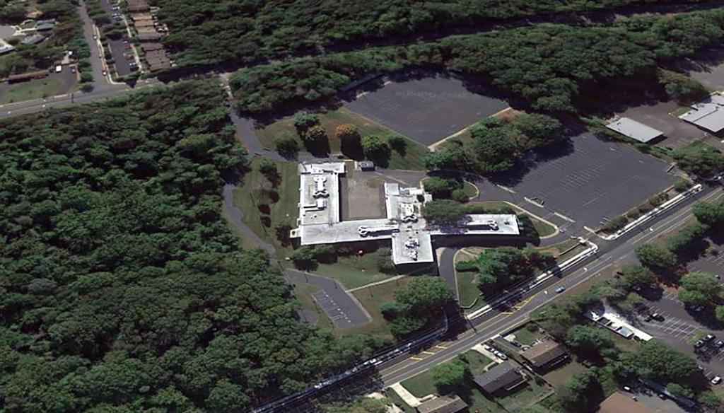 Aerial view of an F-shaped building and parking lot with roads, trees and grassy areas around it