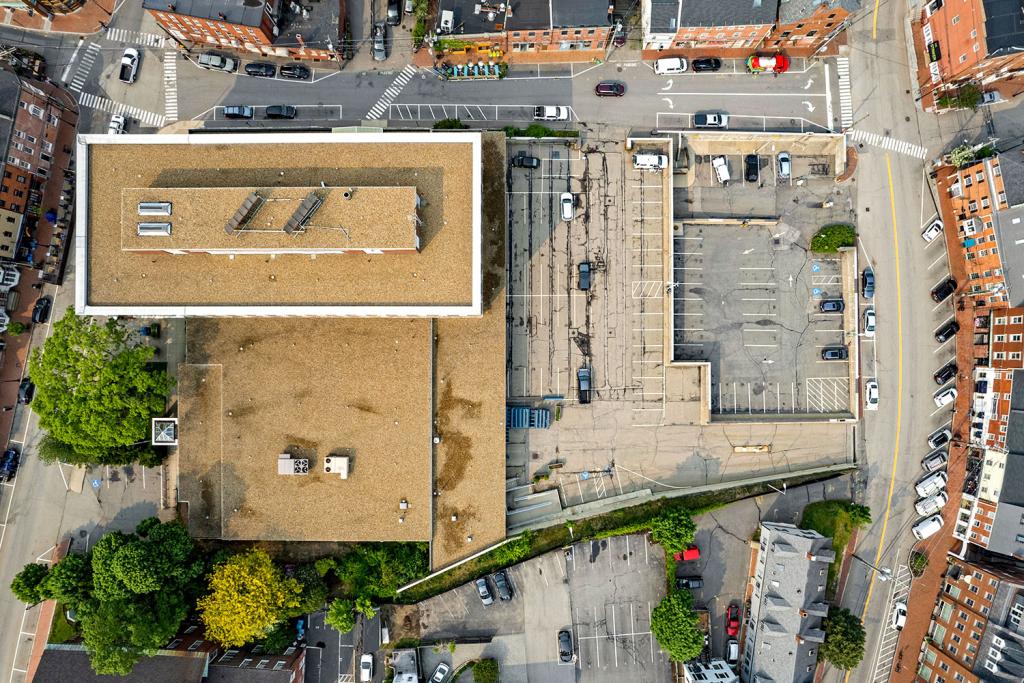 Aerial view of a building on a corner, showing the roof and the parking lot directly from above.