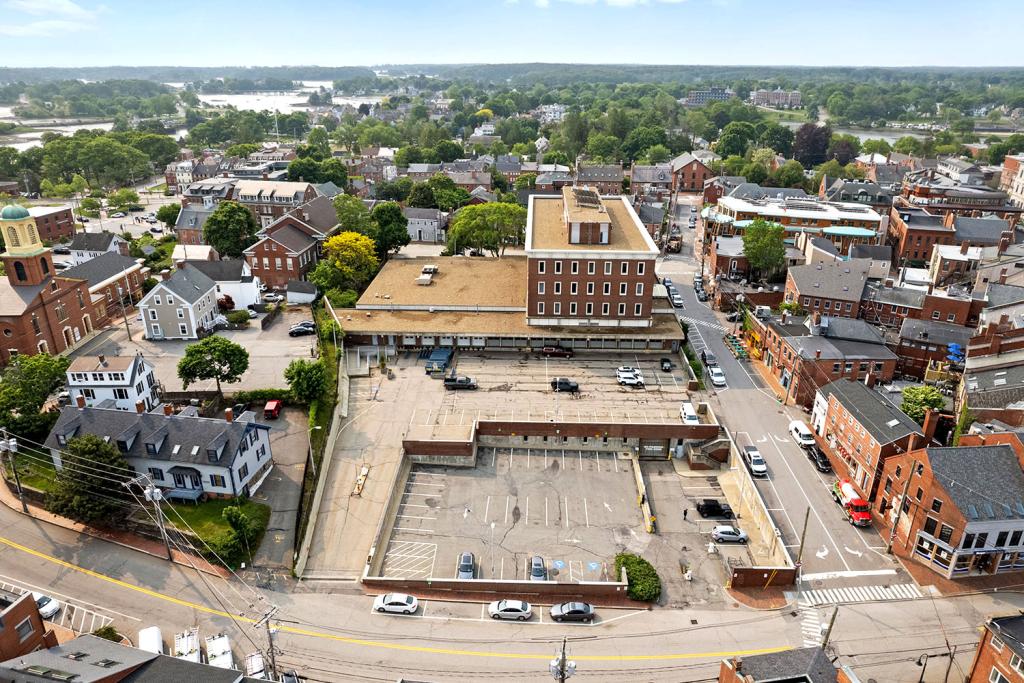 Aerial image of a four-story red brick building with a large one-story annex overlooking a two-level parking lot with loading docks and garage.