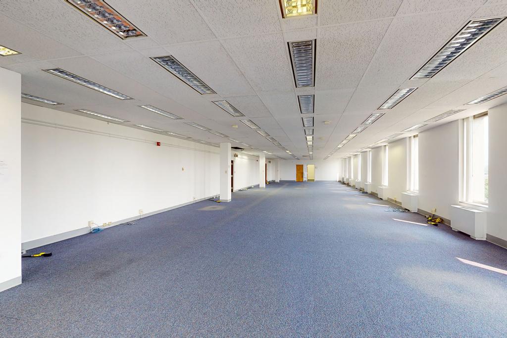 A large open office space with blue carpet and many windows with blinds. 