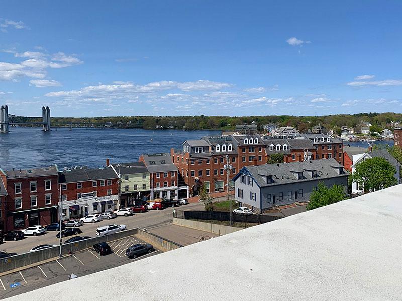 View of a city street with older brick buildings, the Piscataqua River, and a distant bridge.