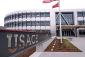 Three level curved silver faceted building facade with partial view of two flags, and USACE sign along walkway to entrance